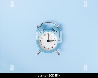 Retro alarm clock middle of blue background. Monochrome simple flat lay with pastel texture. Time concept. Stock photography. Stock Photo