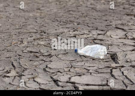 empty crumpled plastic bottle on dry cracked mud desert like gray background Stock Photo