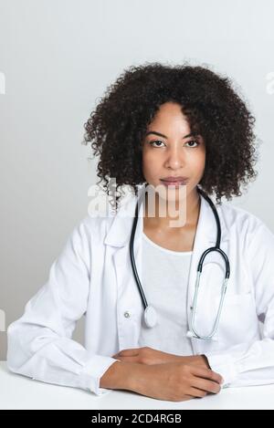 portrait of an attractive afro american doctor with both hands on the top of a white desk. looking at camera Stock Photo