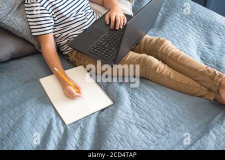 Top view on boy writing or drawing and using his laptop while doing homework. Studying online during quarantine, online training classes or personal Stock Photo