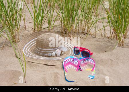 woman's stylish summer hat decorated with seashells in beach sand with sunglasses and flip-flops Stock Photo