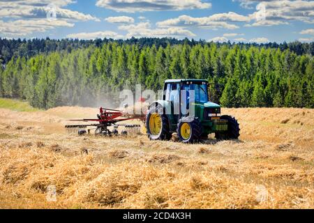 Farmer working in field with John Deere 6420S tractor and Fella rotary rake, raking dry straw on day of late summer. Salo, Finland. August 16, 2020. Stock Photo