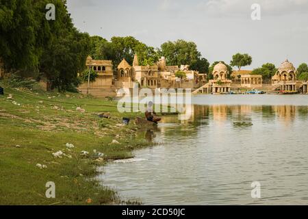 local middle aged man bathing and washing clothes at the shore of a dirty lake Stock Photo