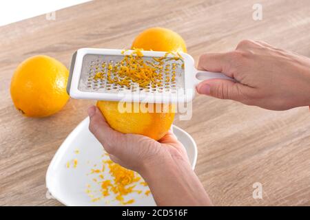 Woman rubbing orange zest with metal grater in the kitchen Stock Photo