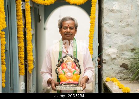 happy Elder man with Ganesha Idol coming home during ganesha or vinayaka Chaturthi festival - Concept of indian religious festival celebration. Stock Photo