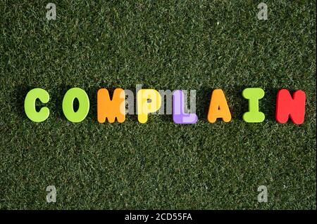Capital letter "Complain" word from colorful of wood on grass background. Stock Photo