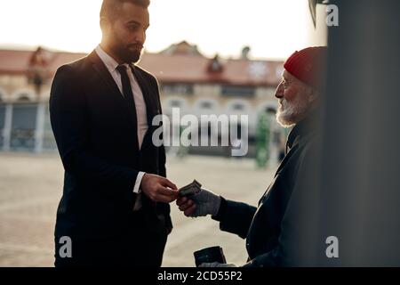 Young business man in suit help vagrant man in street, giving money donation. people relationship and lifestyle concept Stock Photo