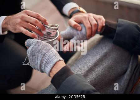 Kind man help beggar male sitting on street , give money donation, Pity male need money, food, shelter. Beggar with grey gloves. Businessman in tuxedo Stock Photo