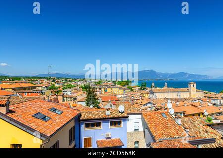 Aerial panoramic view of Desenzano del Garda town with bell tower of Duomo di Santa Maria Maddalena Cathedral church, red tiled roof buildings, Garda Lake, mountain range, Lombardy, Northern Italy Stock Photo