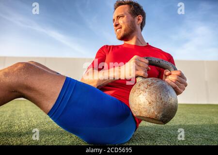Crossfit training athlete man working out doing russian twists abs situp workout with kettlebell heavy weight in outdoor gym Stock Photo