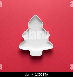 Empty white plate in shaped of Christmas tree on red with space for design. View from above. Stock Photo