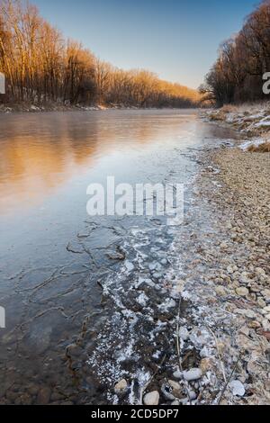 Bank of the river Isar near Garching in Bavaria on sunny cold winter day with ice, trees and snow Stock Photo
