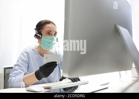 Remote work. A woman in a surgical mask works on the computer. Work during the plague Quarantine. Working at the computer in a mask. protection of emp Stock Photo