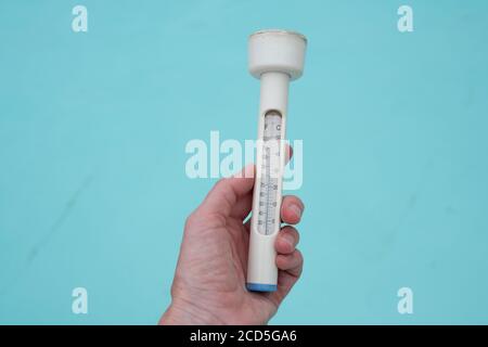 Mans hand holding a thermometer against background of swimming pool Stock Photo