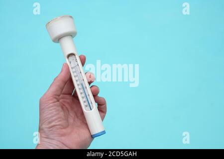 Mans hand holding a thermometer against background of swimming pool Stock Photo