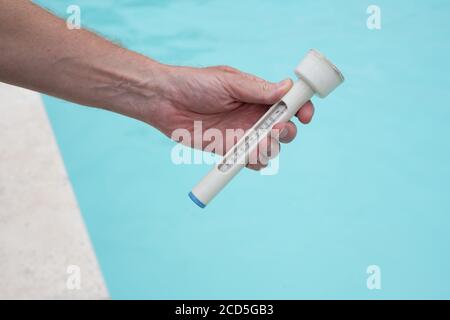 Mans hand holding a thermometer against background of swimming pool Stock Photo