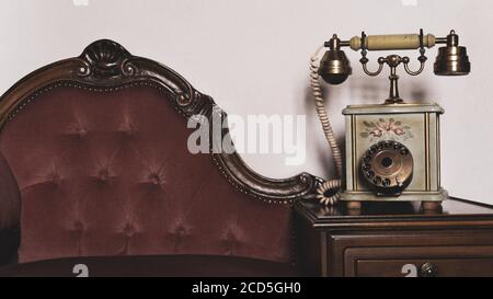 Elegant vintage old telephone on elegant wooden upholstered sofa against white wall.Relaxing antique room interior vintage decoration Stock Photo