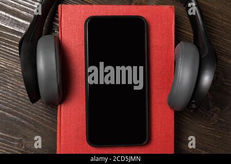 Mobile phone on the book with headphones. Concept of audio books. Top view closeup Stock Photo