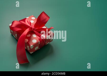 Holiday gift in red and white packaging with polka dots and red bow on green. Xmas present. Stock Photo