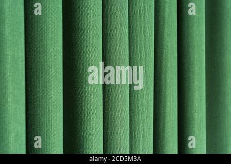 Closeup view of green curtain in thin and thick vertical folds made of dense fabric.Textured materials and textiles abstract backgrounds. Stock Photo