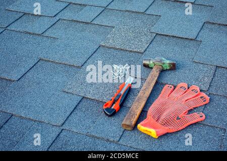 Close up view on asphalt shingles on a roof  with hammer,nails and stationery knife. Stock Photo