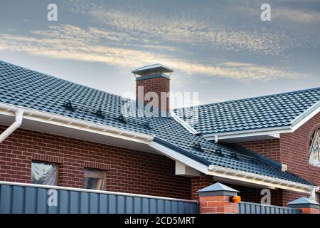 Newly installed construction frame house rain gutter system on the metal roof top. Brick chimney pipe. Automatic metal gates. Stock Photo