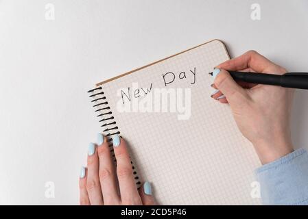 Notepad with words New Day on white background. Female hands writing in copybook. Top view copy space. Stock Photo