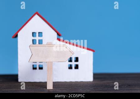 Home model with wooden signboard. Buying house concept. Blue background, front view. Stock Photo