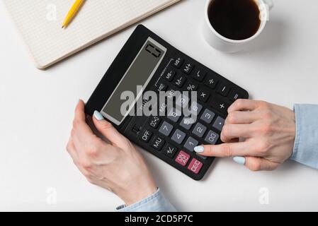 Woman using calculator. Documents, cup of coffee and calculator on a white background. Top view. Stock Photo