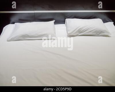 Two rectangular pillows in white pillowcases lie on a white sheet Stock Photo