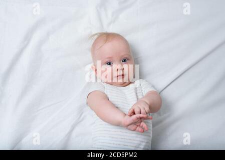 Portrait of a cute 3 months baby lying down on white blanket. Happy child looks into the camera. Stock Photo
