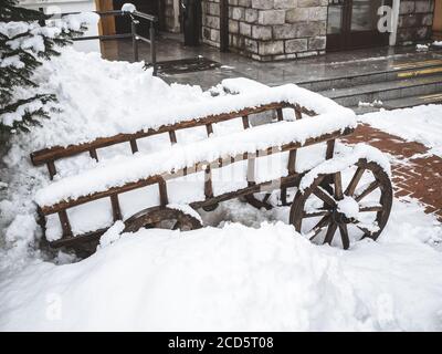 A wooden cart covered with snow stands in a snowdrift next to a stone building with marble steps Stock Photo