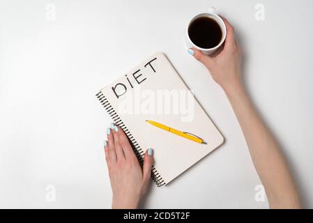 Female hand holding a cup of coffee, a notebook with the title Diet. Preparation menu concept. Stock Photo