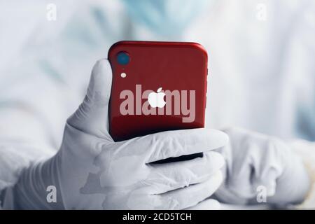 Person holds red apple iphone in gloves closeup. Bishkek, Kyrgyzstan - March 14 2020. Stock Photo