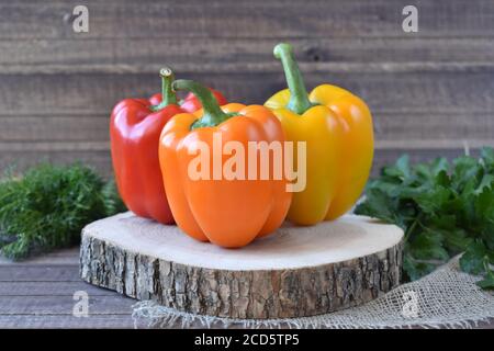 Three peppers on a wooden stand in the background of dill and parsley. Grass for salad. Stock Photo