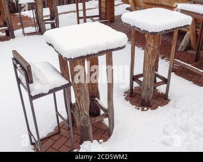 Tall wooden tables and bar stools of an outdoor cafe stand covered with snow in winter Stock Photo