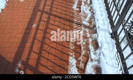 Red paving slabs with melting snow and footprints on it and shadow from the railing Stock Photo