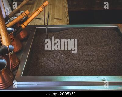 Sand for making an oriental coffee with a metal spoon in it and many Turks standing on the side Stock Photo