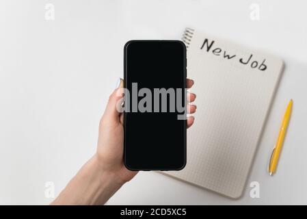 Female hand holds the phone. Pen and notebook with words New job. White background copy space. Stock Photo