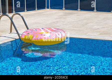 pink inflatable donut doughnut floating mattress in swimming pool. Beach pool accessories. Summer holiday concept Stock Photo