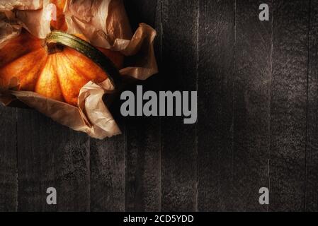 Flat lay image of a mini decorative pumpkin wrapped in plain brown paper with warm side light. Horizontal with copy space. Stock Photo