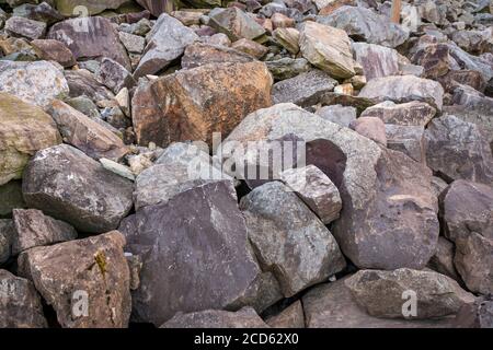 Heavy rocks and boulders of different shades of greys and browns lay piled on a hill. Stock Photo