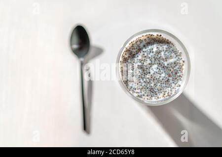 Chia seeds pudding in almond milk - healthy vegan eating breakfast in morning. Top view of kitchen table with black spoon and glass cup Stock Photo