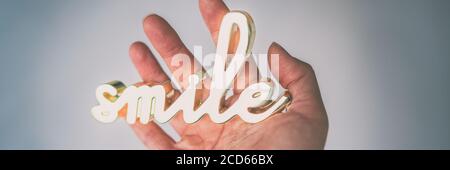 Hand holding smile sign written in metal gold. Text decoration for home or office motivational quote for happiness. Banner panorama background Stock Photo