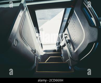 A wide-angle view with selective focus from inside of a regular intercity bus entrance with opened door and with steps with yellow borders, a door to Stock Photo