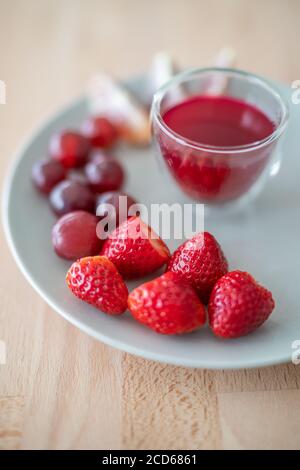 Red fruits plate presentation of healthy breakfast fruits juice with strawberries, red grapes, blood orange wedges. Juicing detox concept Stock Photo
