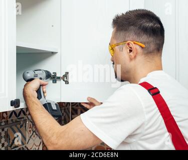 Service contractor using electric screwdriver while installing new furniture in kitchen Stock Photo