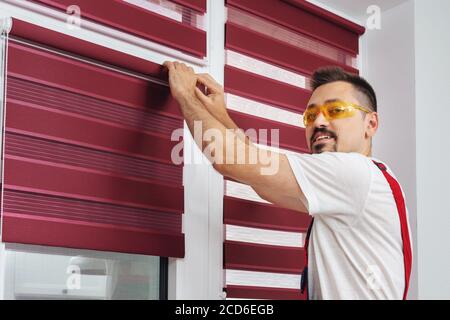 Construction worker man in a uniform install blinds look at camera and smiling Stock Photo