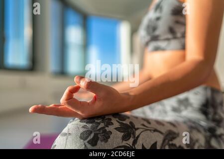 Yoga class at gym studio woman meditating with hand mudra in lotus pose in morning sun. Yoga practice meditation healthy living at home lifestyle Stock Photo