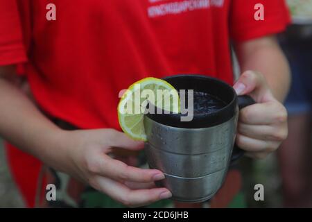 Children's hands hold a red mug with tea in the autumn park Stock Photo